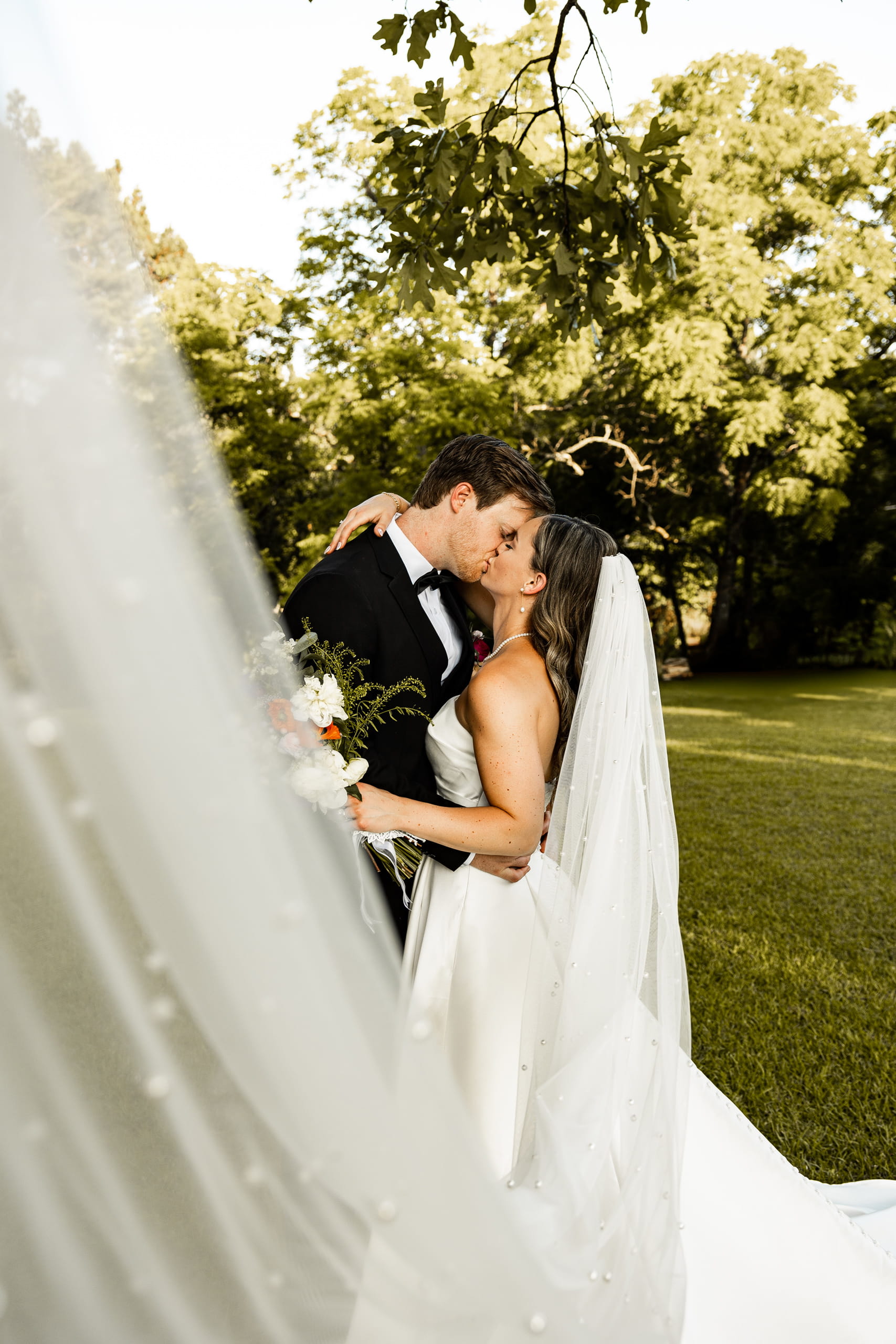Andrew and Alyssa holding each other in their arms and kissing, wrapped in the bride’s flowing veil for a tender and intimate moment.