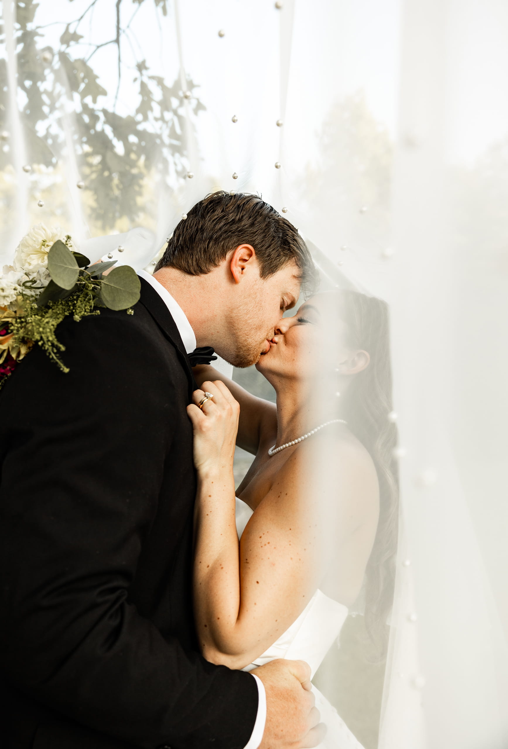 Bride and groom kissing under the bride’s veil, holding each other in a romantic wedding portrait.