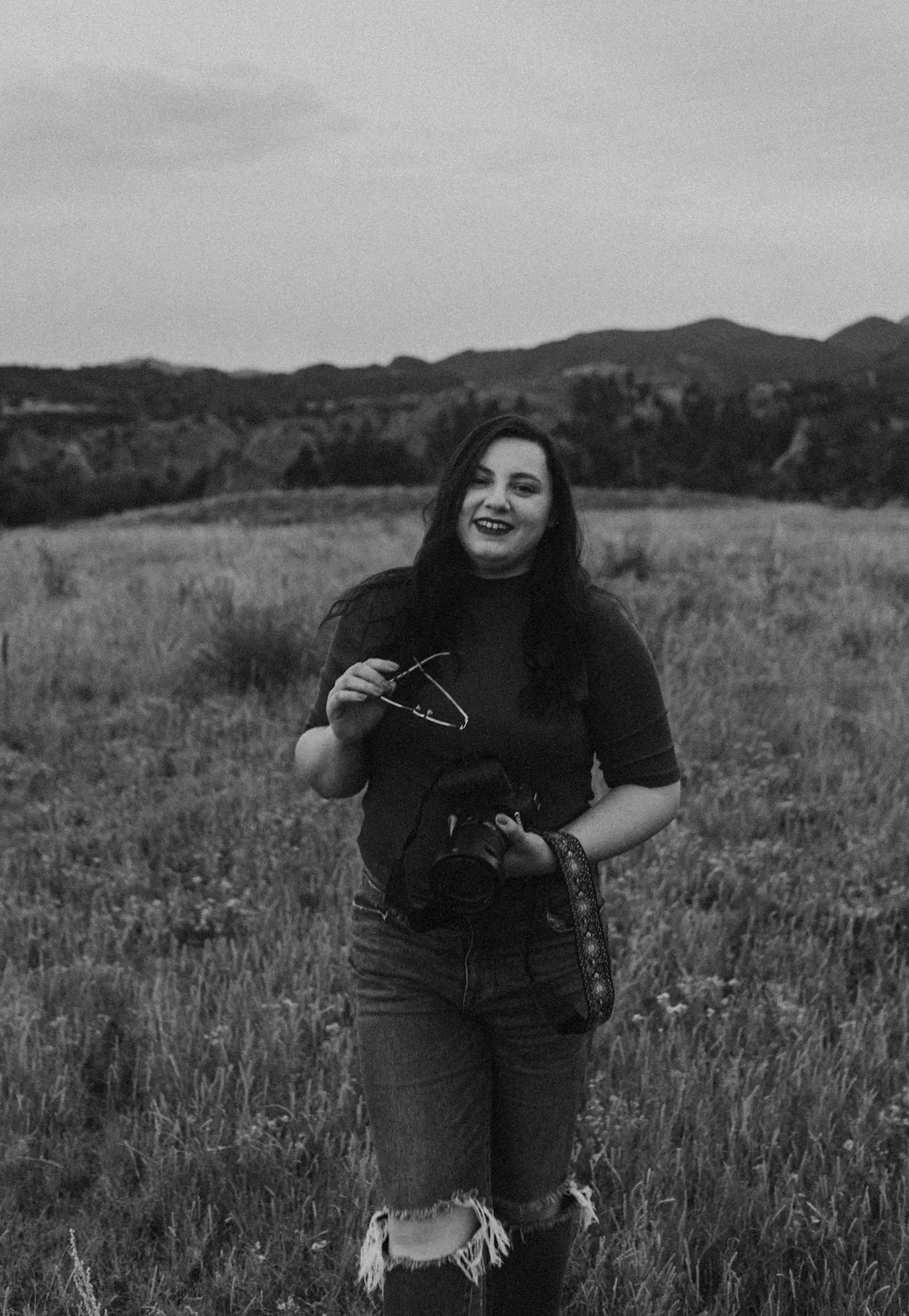Black and white portrait of Mădălina Price, destination and adventure elopement wedding photographer, standing outdoors surrounded by nature.