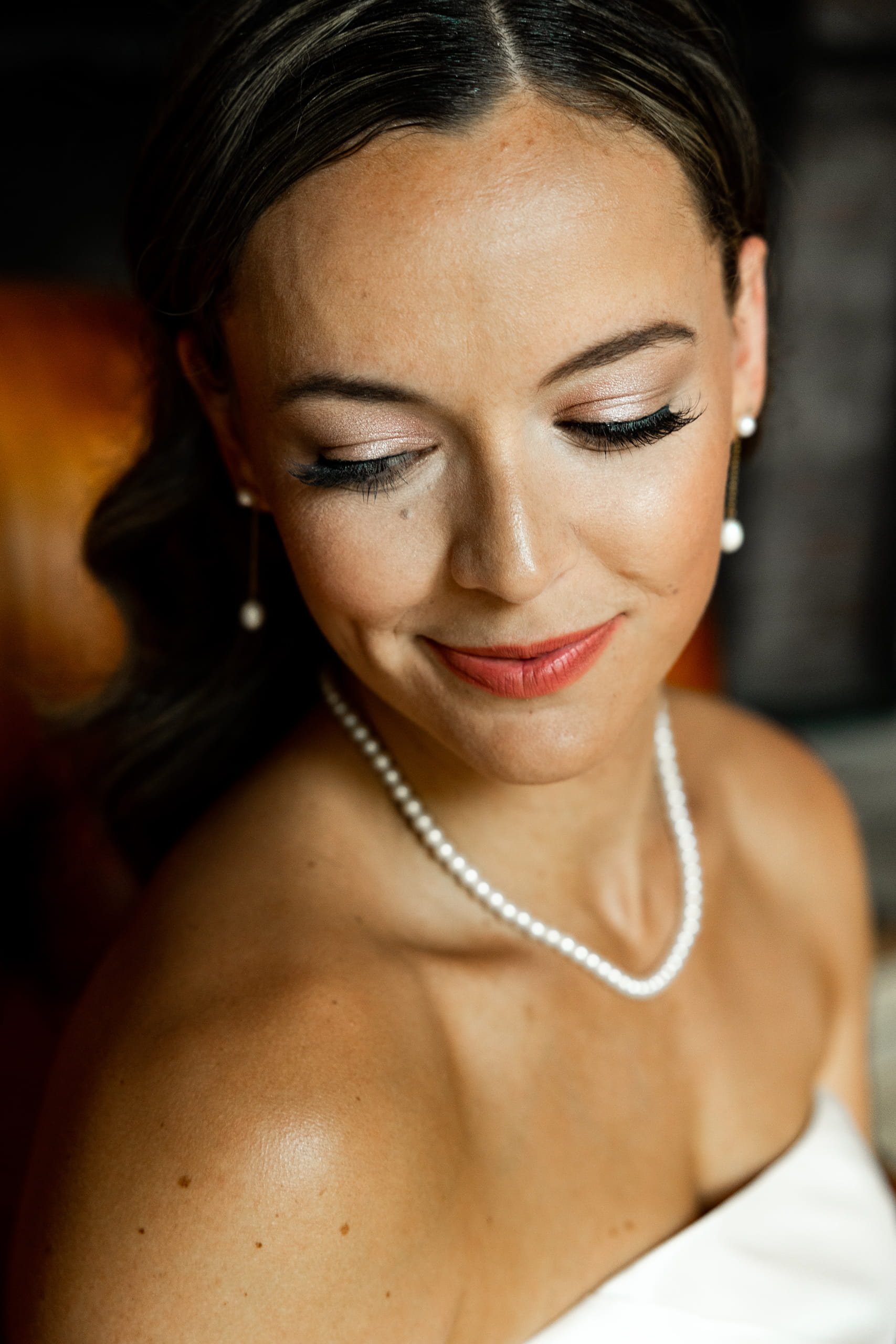 Bride with elegant makeup and pearl necklace, highlighting her face, tanned skin, and a glimpse of the wedding dress.