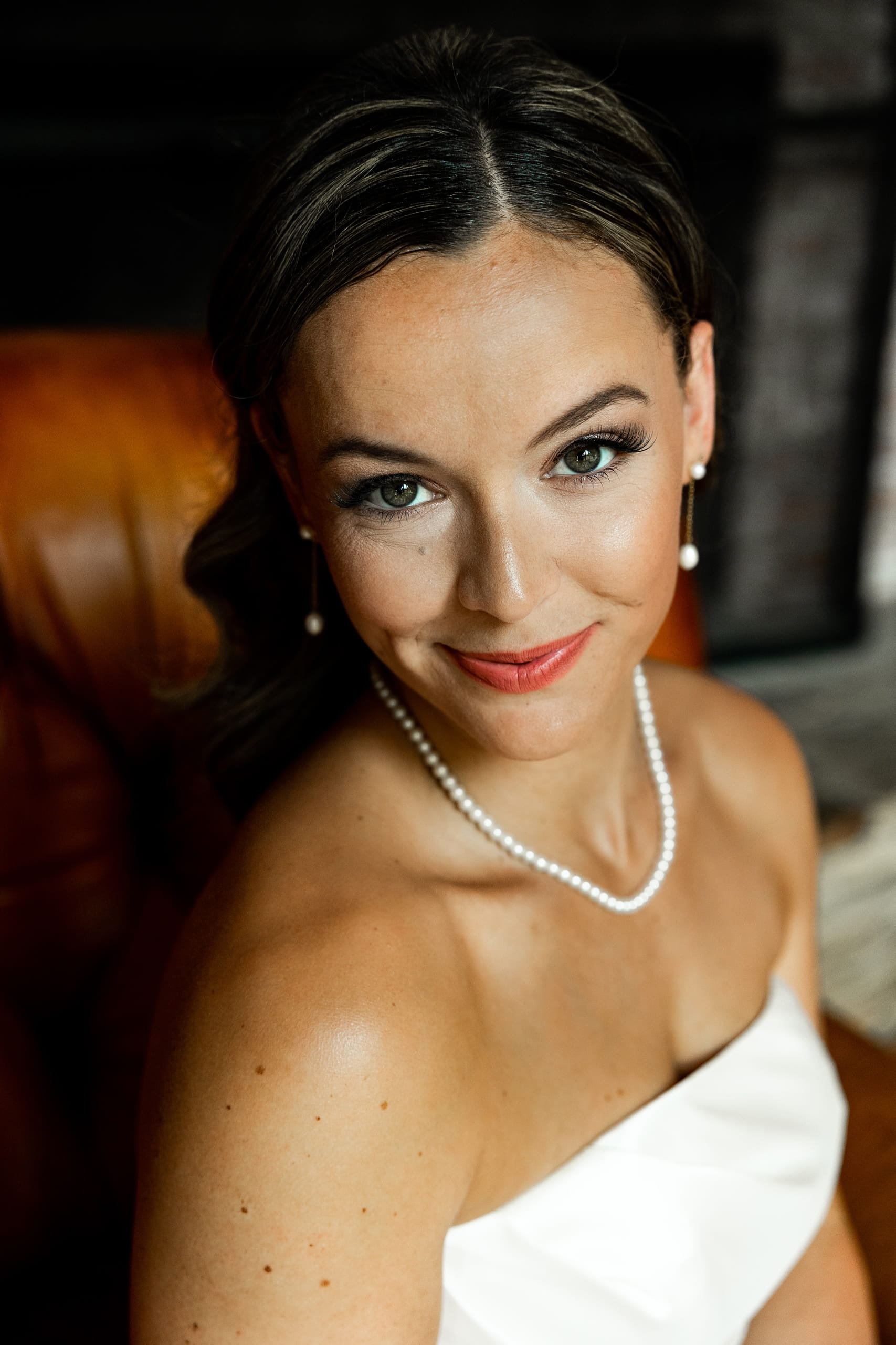 Close-up portrait capturing the bride’s gentle smile and expressive eyes, adorned with pearl earrings and elegant bridal styling.