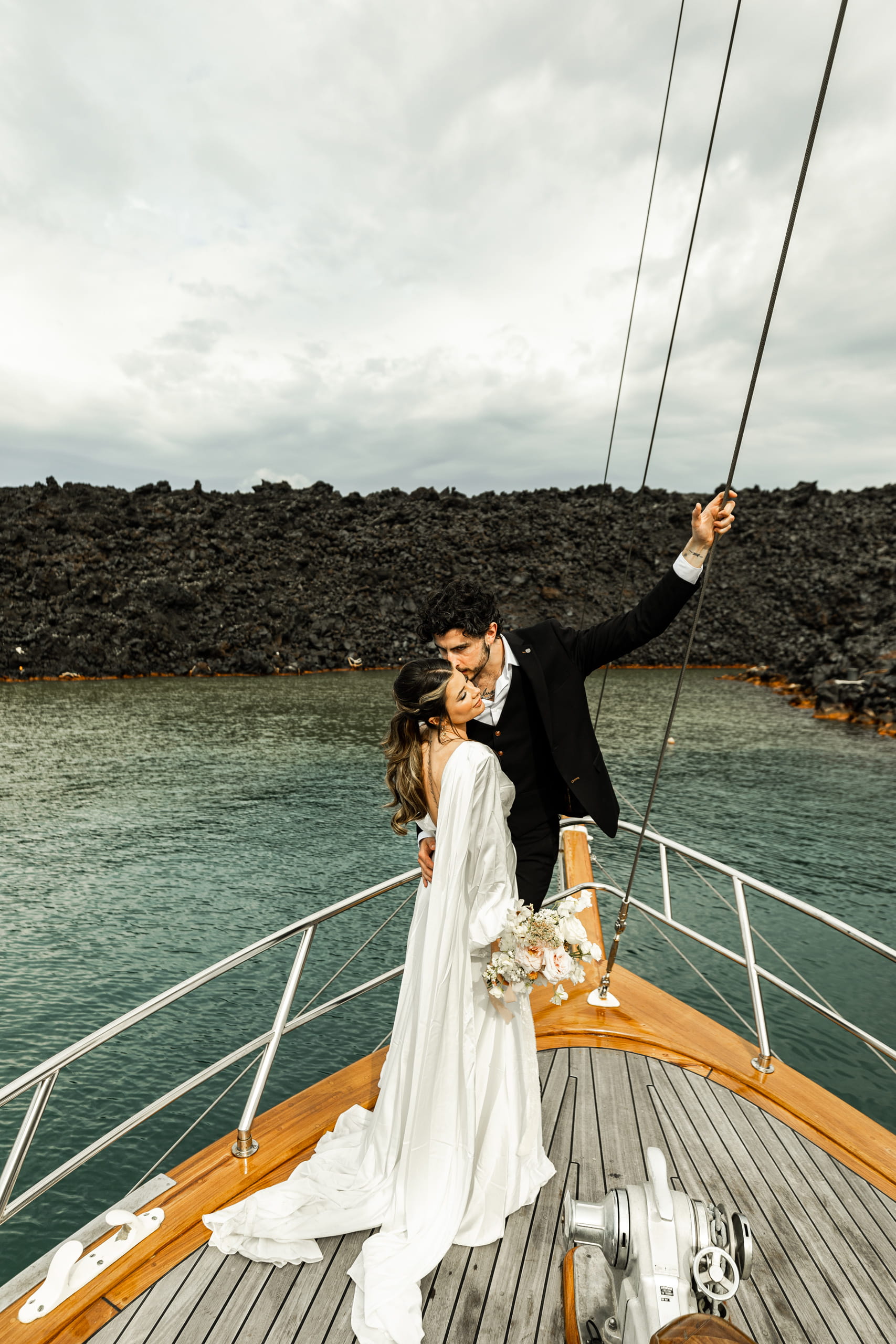Jeannie and Matty sailing across the Aegean Sea in Santorini, celebrating their love amid volcanic cliffs and serene sea views.