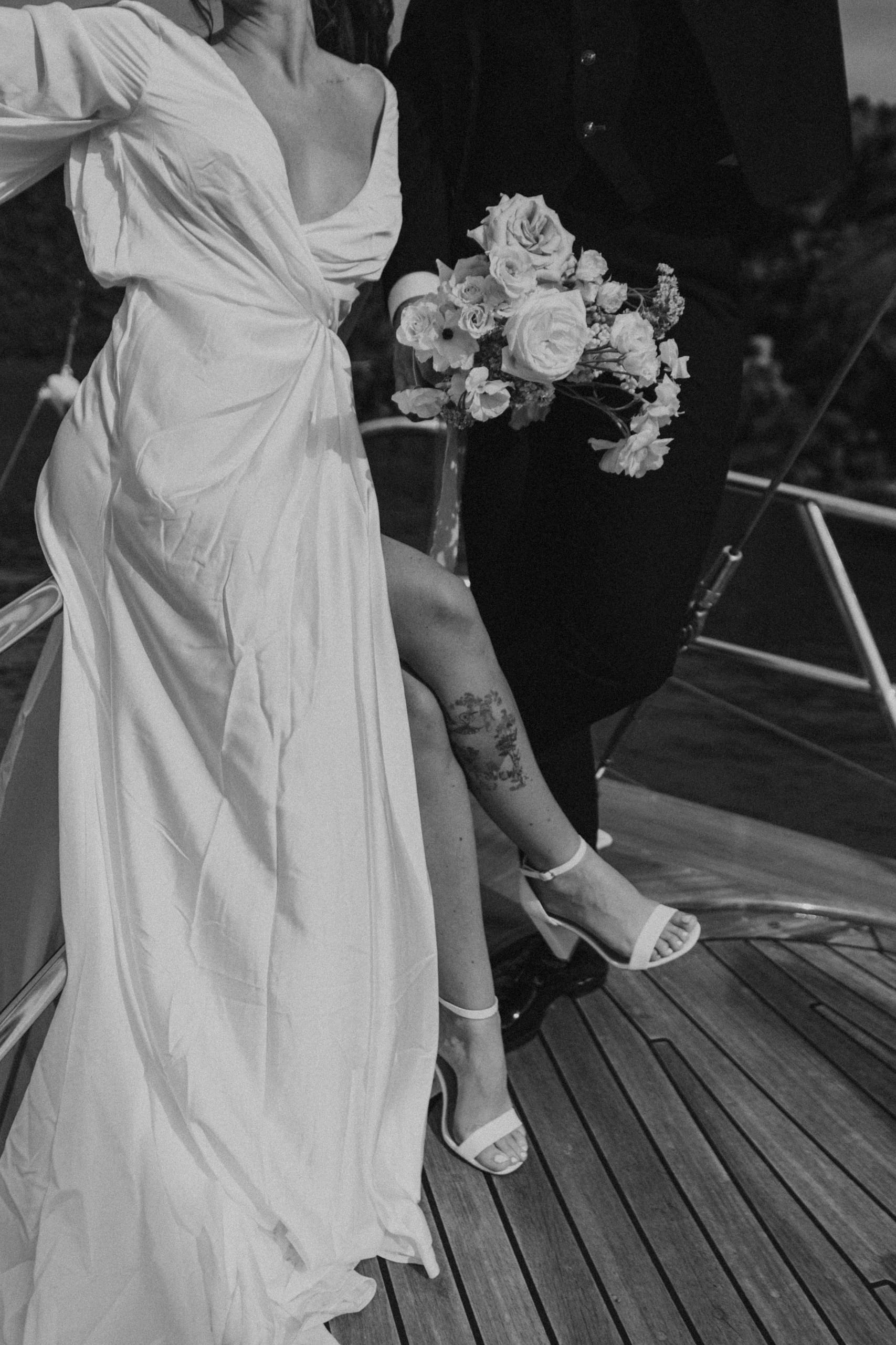 Black and white photo highlighting Jeannie’s leg tattoo in her wedding dress, a fine-art detail from her Santorini elopement with Matty.