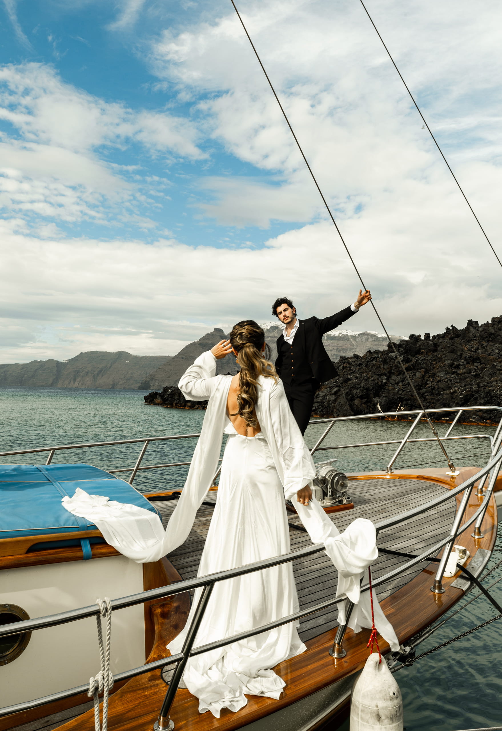Matty standing at the front of the sailboat waiting for Jeannie, with Santorini’s blue and white sky stretching endlessly above them.