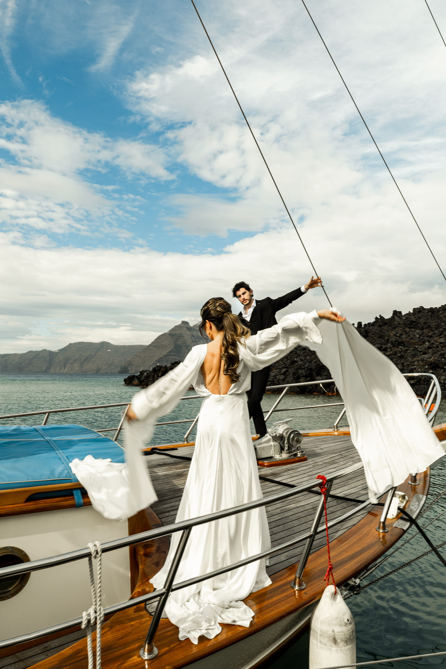 Bride Jeannie opening her arms wide as she walks toward Matty on the sailboat, capturing a joyful and cinematic Santorini elopement moment.