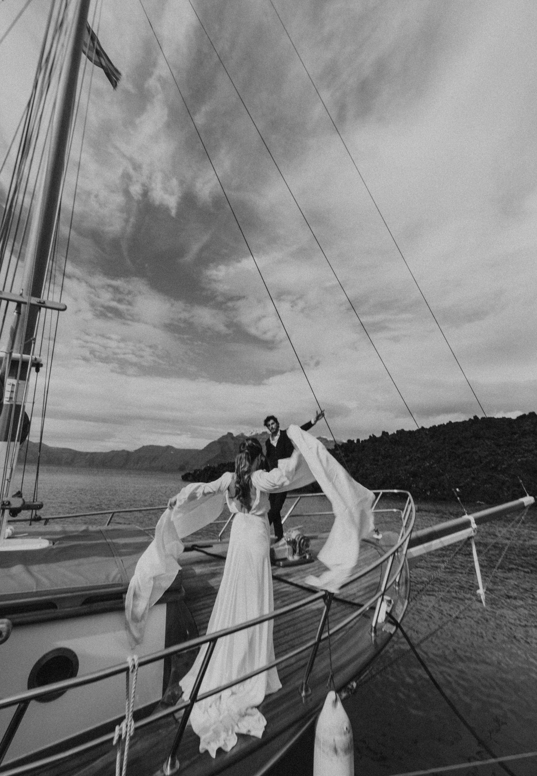Black and white photo of Jeannie opening her arms wide as she walks toward Matty on the boat, capturing a timeless and emotional Santorini elopement moment.