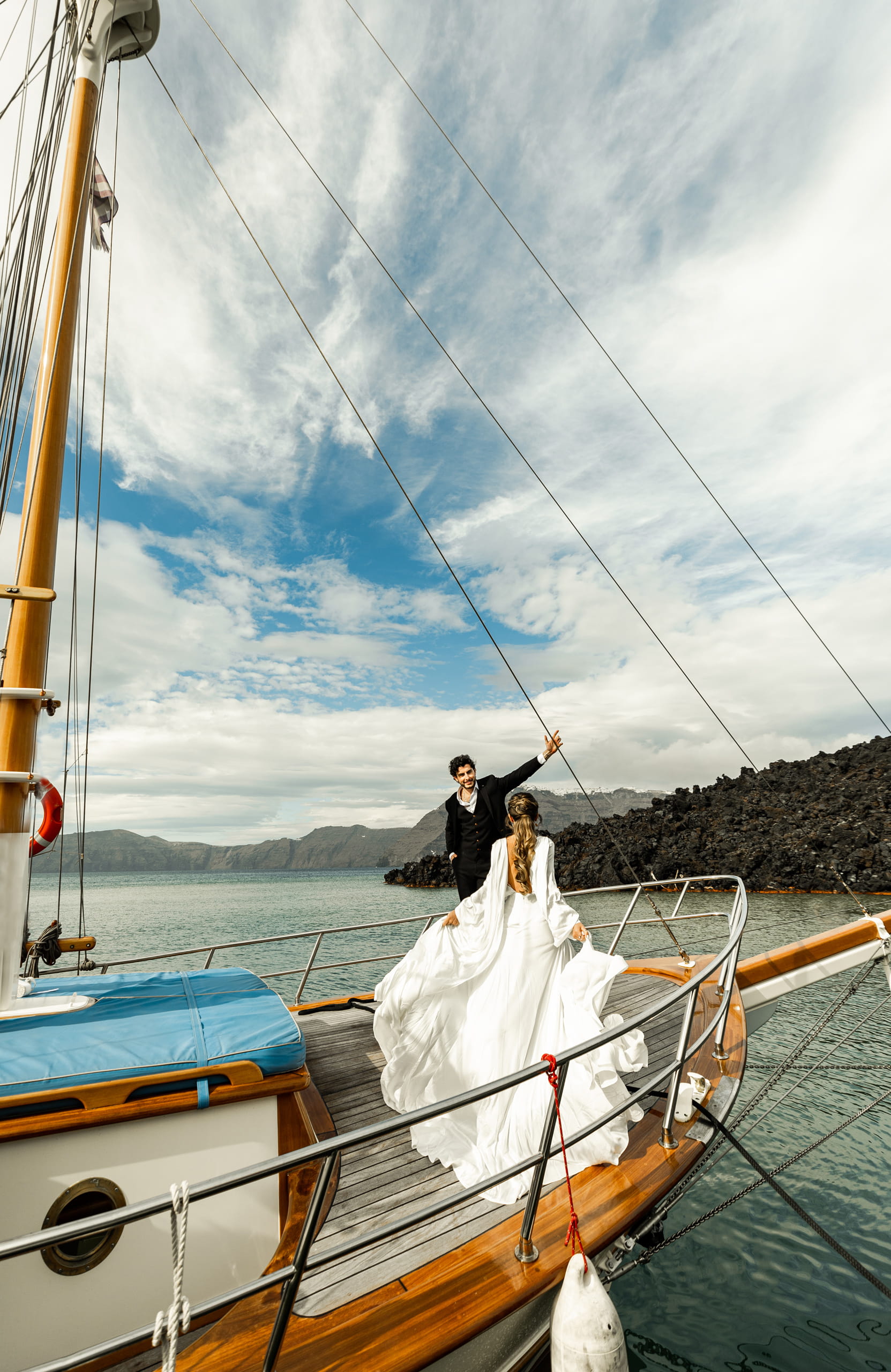 Matty waiting at the front of the sailboat in Santorini as Jeannie lifts her wedding dress and walks gracefully toward him across the deck.