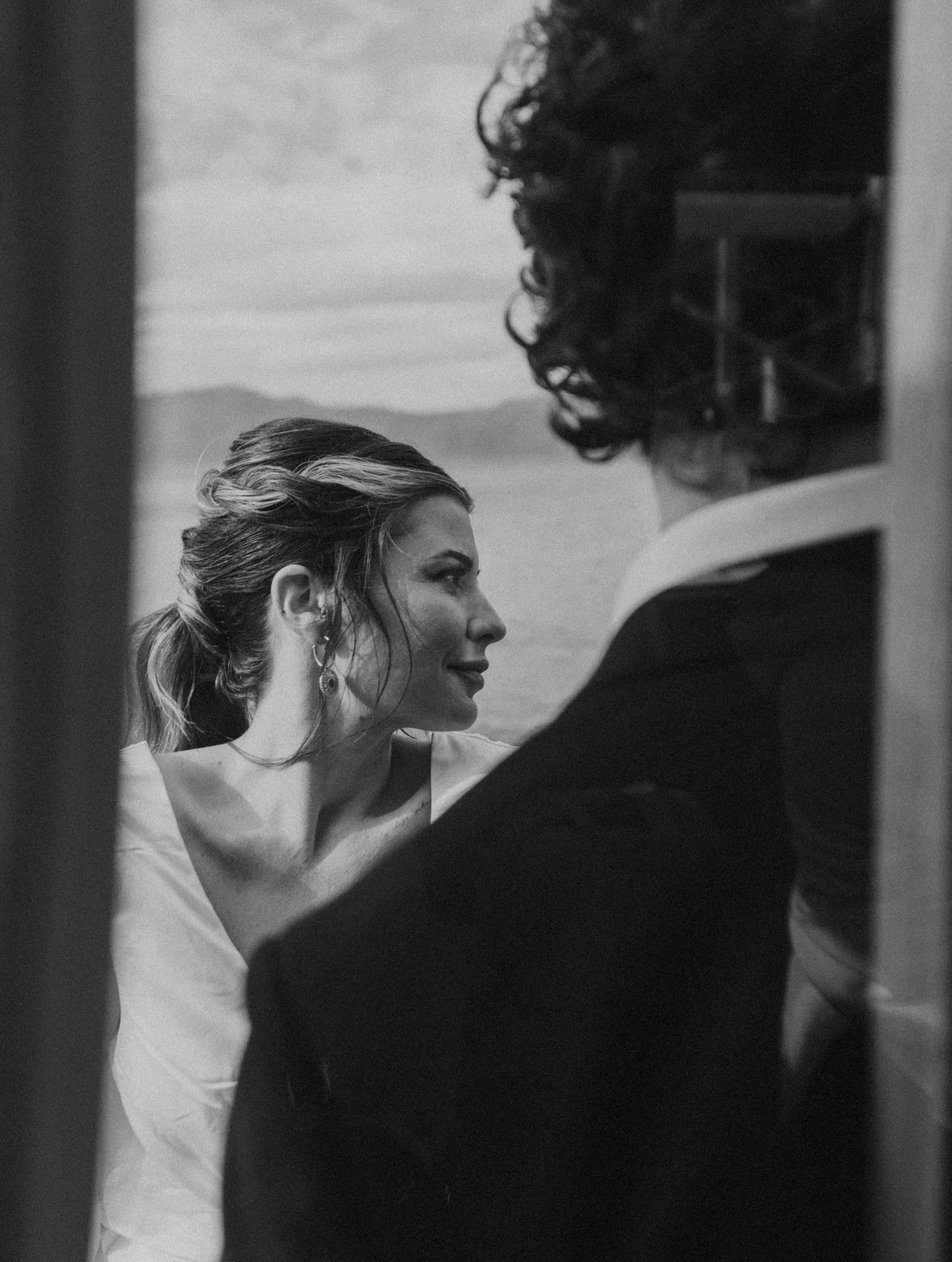 Artistic black and white close-up of Jeannie on the side of the sailboat, gazing toward the horizon during her Santorini elopement with Matty.