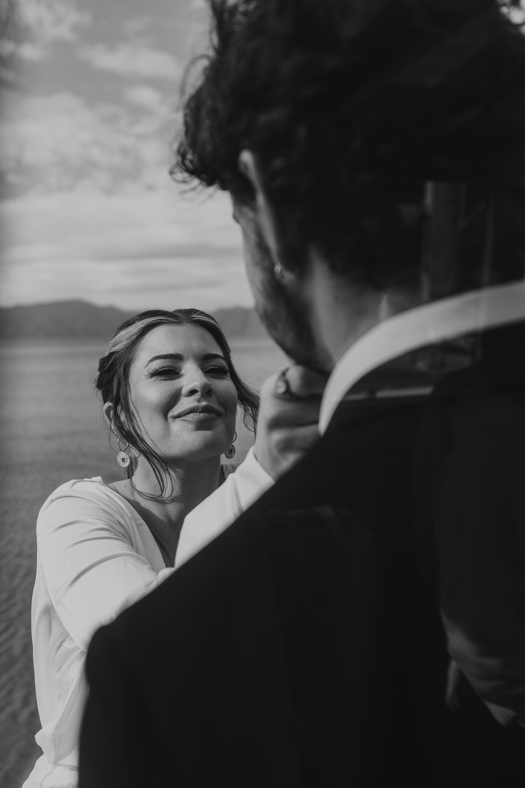 Black and white portrait of Jeannie on the sailboat, her eyes turned lovingly toward Matty in a timeless and romantic Santorini wedding moment.