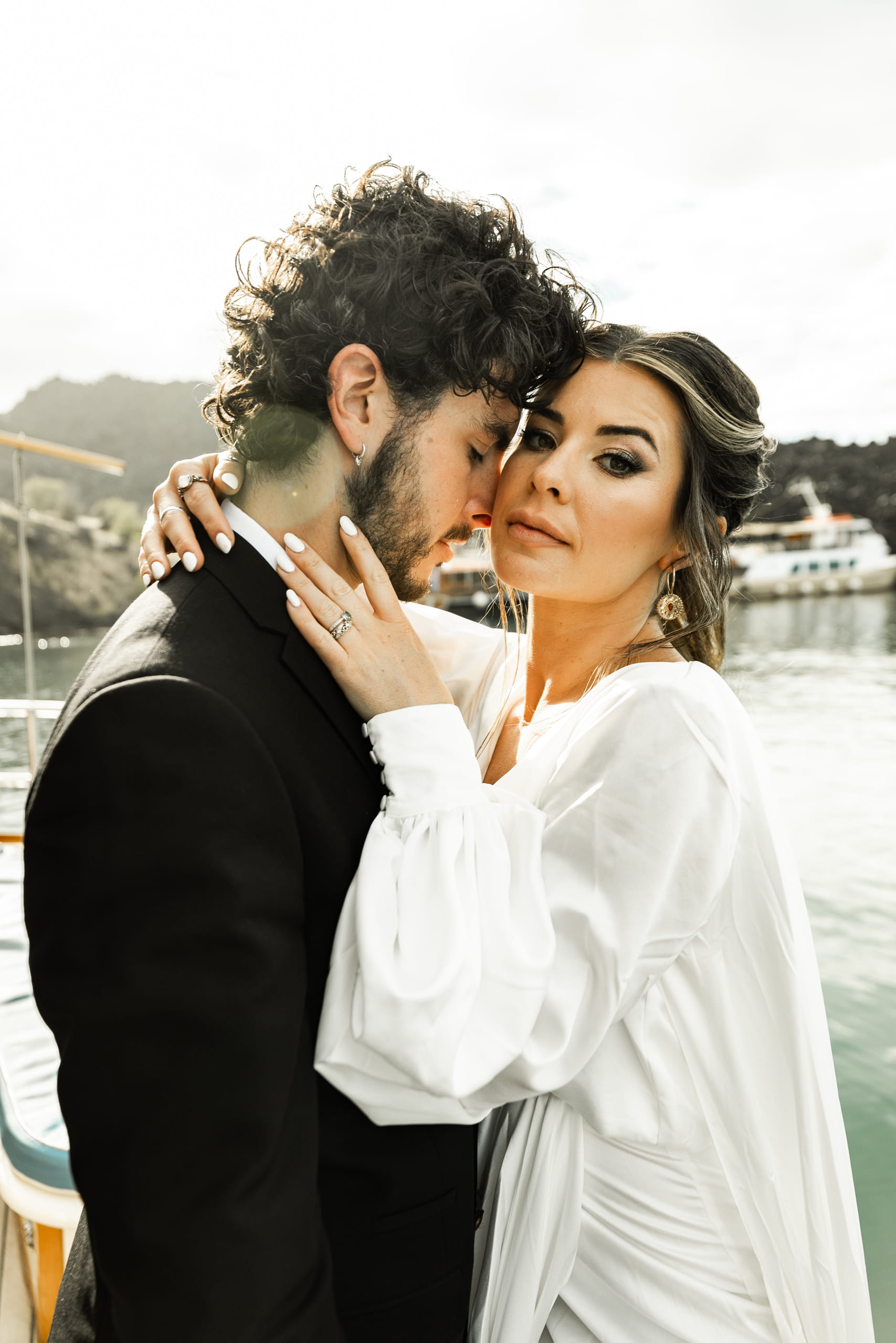 Close-up of Jeannie and Matty embraced on their sailboat in Santorini, a soft and intimate portrait of love and serenity.