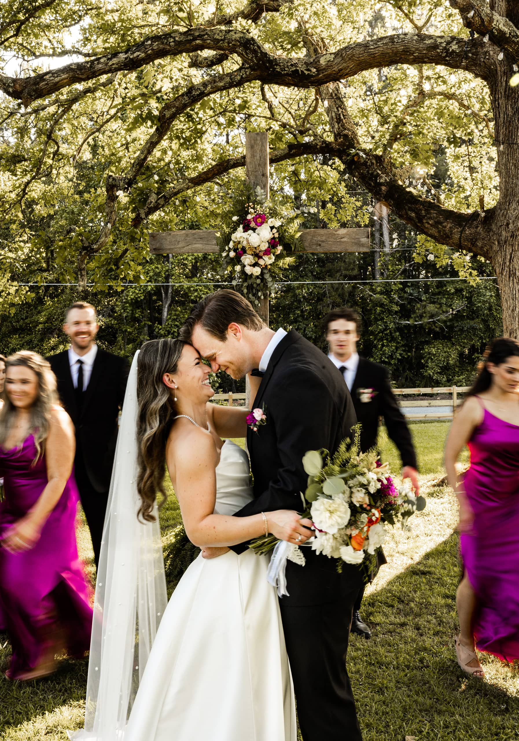Andrew and Alyssa about to kiss, with their bridesmaids and groomsmen softly blurred in the background as they walk away.